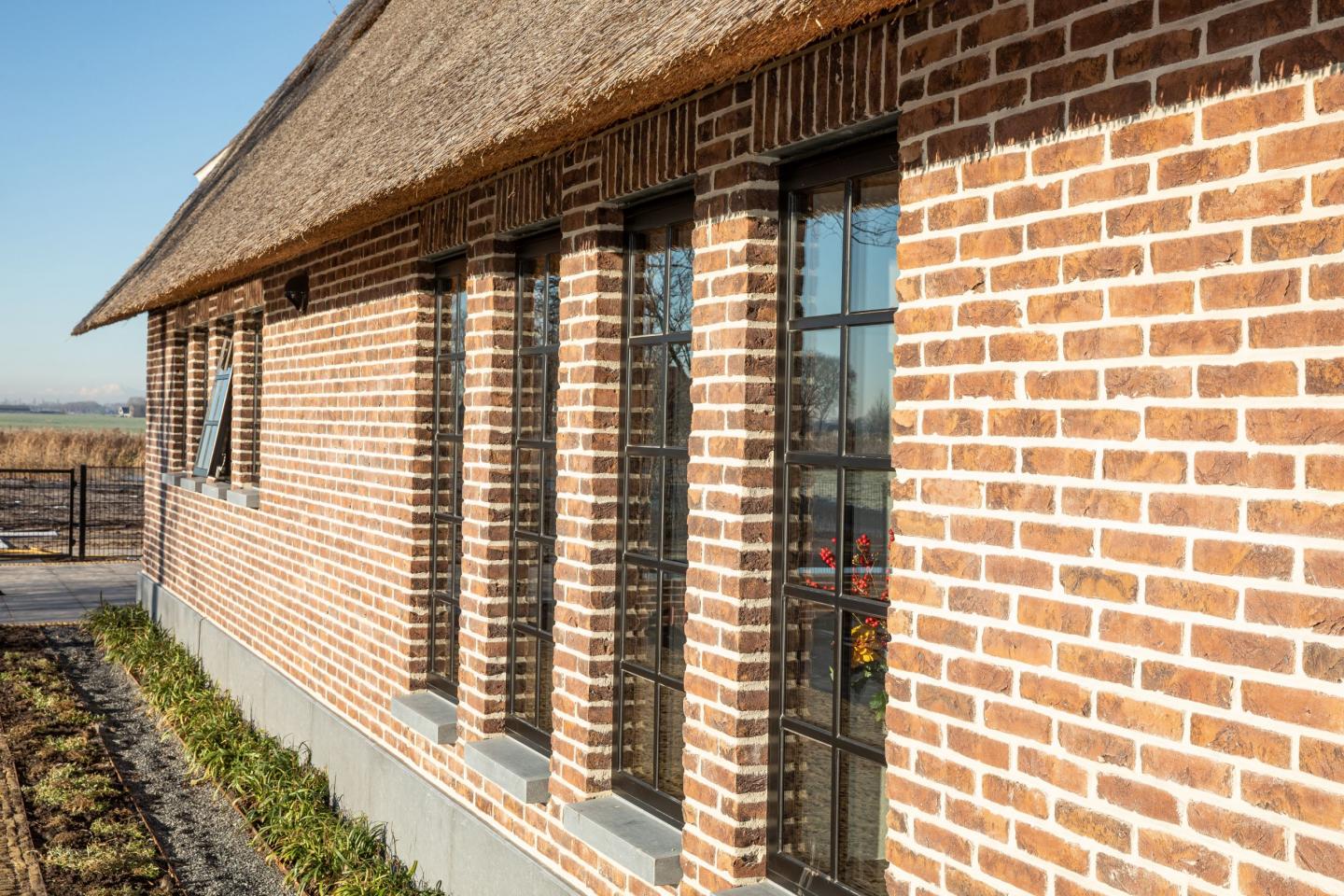 Vier hoge ramen met zwarte kozijnen in een nieuwe woonboerderij